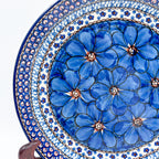 UNIKAT Cobalt Poppies plate, angled close-up view of blue poppy cluster and dotted border displayed on stand
