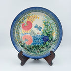 UNIKAT Garden Delight plate, front view displayed on wooden stand showing pom-pom flowers and dragonfly