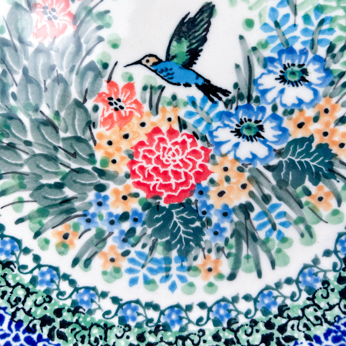 UNIKAT Hummingbird Meadow plate, close-up view of hummingbird perched among red peony and blue flowers