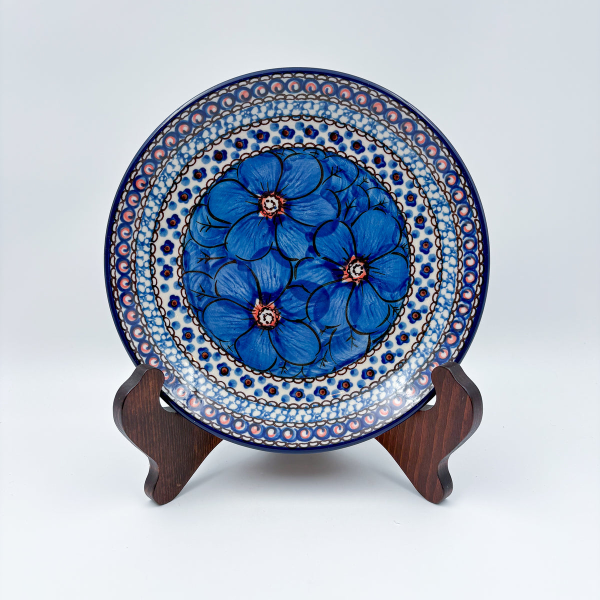 UNIKAT Cobalt Poppies dessert plate, front view displayed on wooden stand showing blue poppy cluster