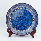 UNIKAT Cobalt Poppies plate, front view displayed on wooden stand showing blue poppy cluster and scalloped border