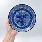 UNIKAT Deep Winter plate held in hand, front view showing blue pansy cluster and rose border