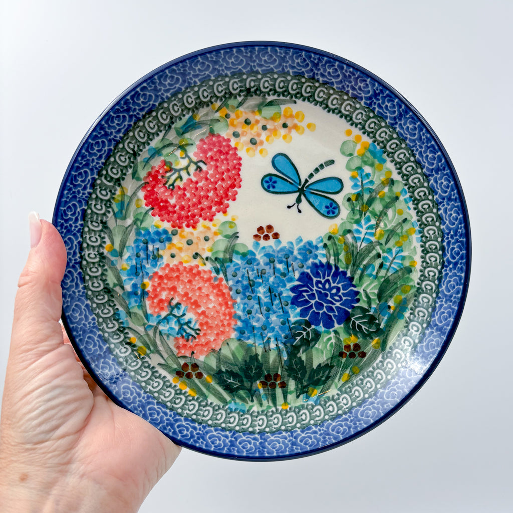 UNIKAT Garden Delight plate held in hand, front view showing pom-pom flowers, dahlia, and dragonfly