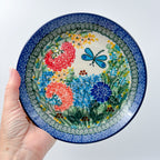 UNIKAT Garden Delight plate held in hand, front view showing pom-pom flowers, dahlia, and dragonfly