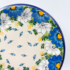 UNIKAT Blue Petal Dance plate, close-up rim view showing blue and white daisies with scattered petal accents