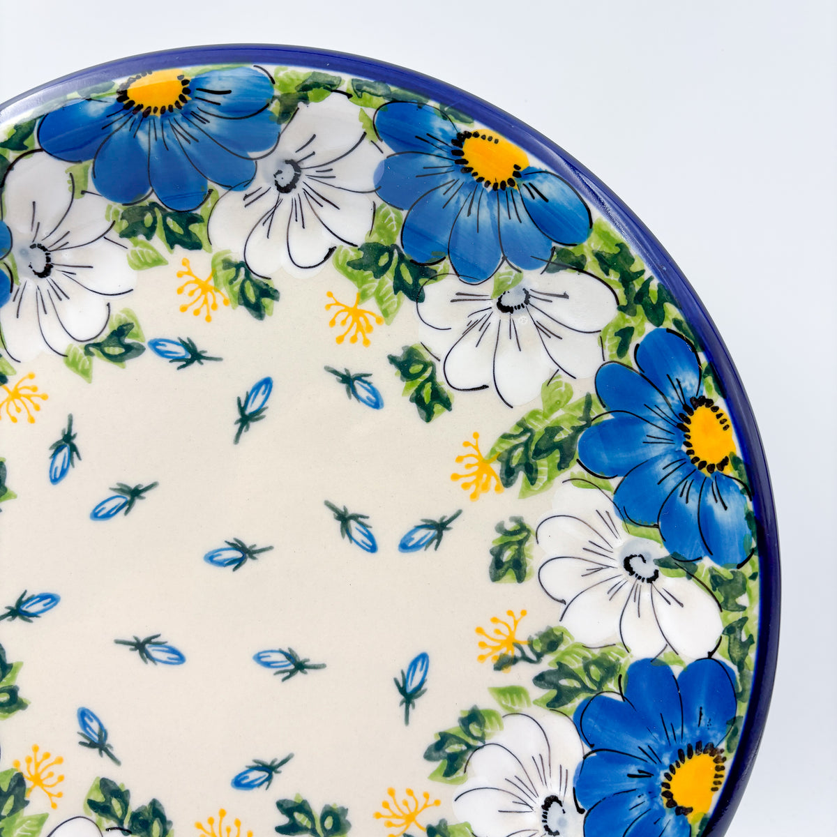 UNIKAT Blue Petal Dance plate, close-up rim view showing blue and white daisies with scattered petal accents