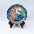 UNIKAT Garden Delight plate, front view displayed on wooden stand showing pom-pom flowers and dragonfly