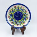 UNIKAT Meadow Breeze plate, front view displayed on wooden stand showing blue wildflower ring around navy center
