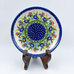 UNIKAT Meadow Breeze plate, front view displayed on wooden stand showing blue wildflower ring around navy center