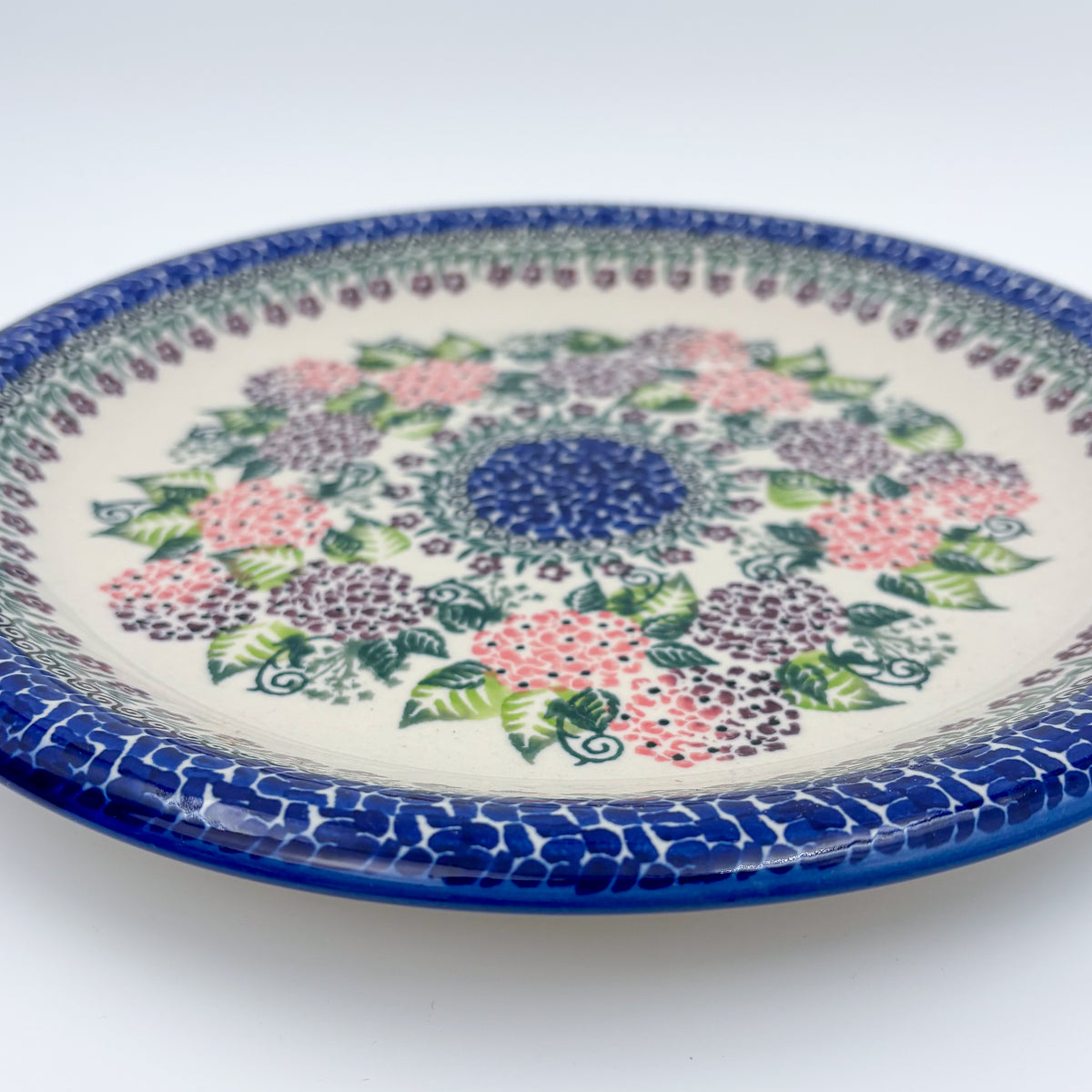 UNIKAT Happy Hydrangea plate, angled front view showing hydrangea ring and blue mosaic border