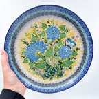 UNIKAT Blue Hydrangea plate held in hand, front view showing hydrangea bouquet and butterfly
