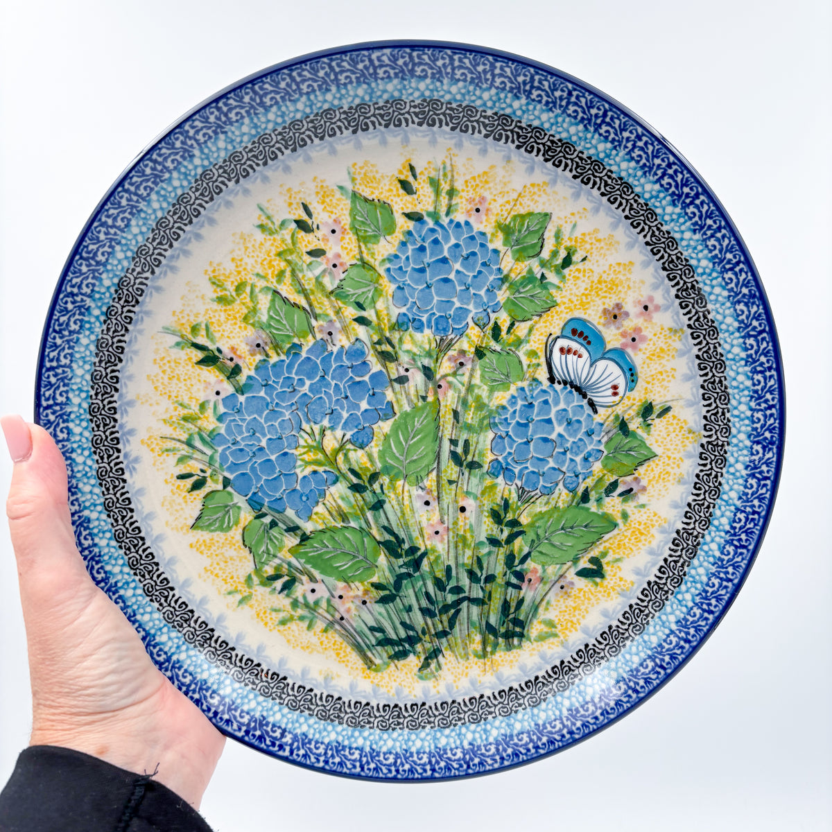 UNIKAT Blue Hydrangea plate held in hand, front view showing hydrangea bouquet and butterfly