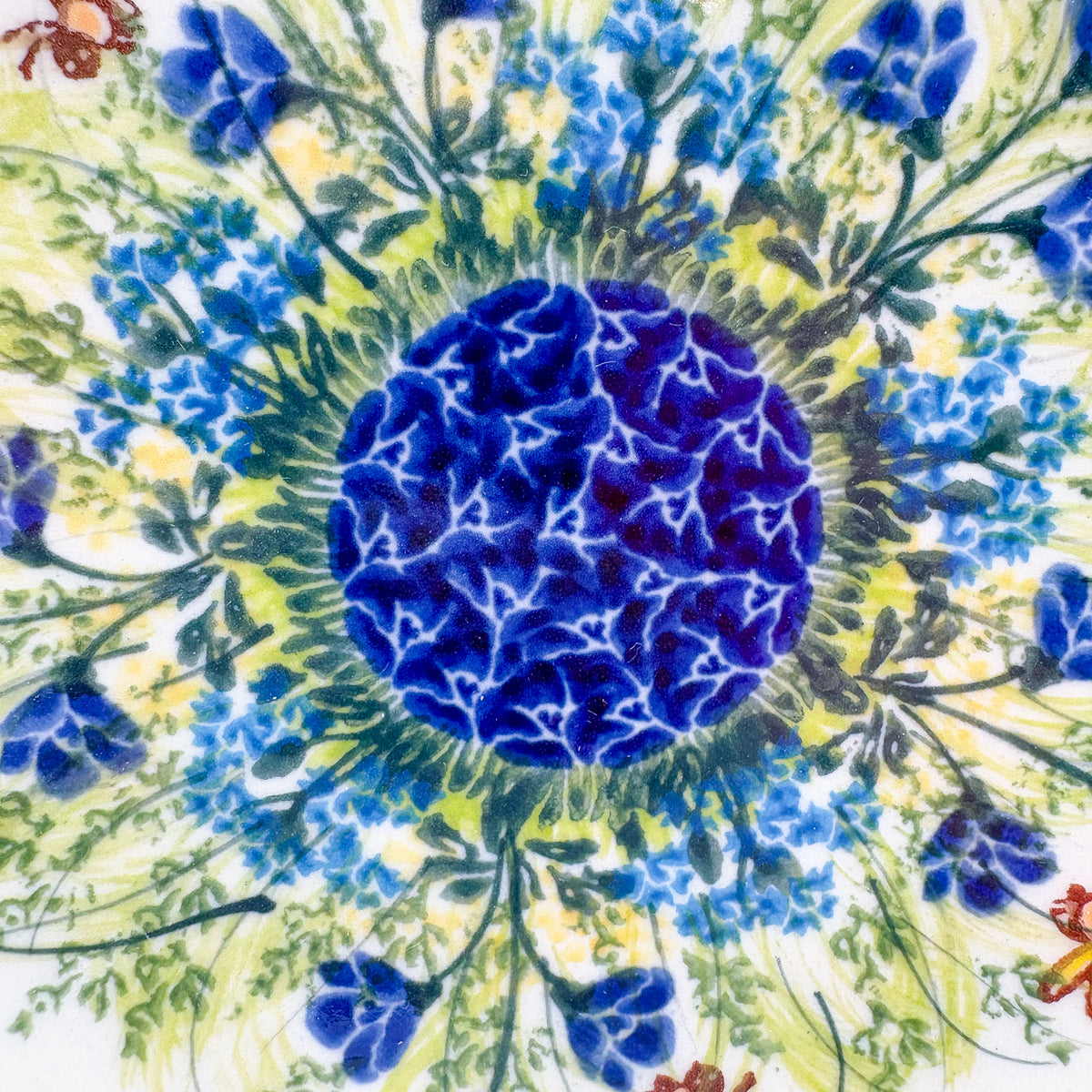 UNIKAT Bluebell Meadow plate, close-up top-down view of navy mosaic center surrounded by blue bellflowers