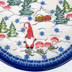 UNIKAT Gnome Village plate, close-up view of gnome, cabin, pine trees, and mushrooms in snow scene