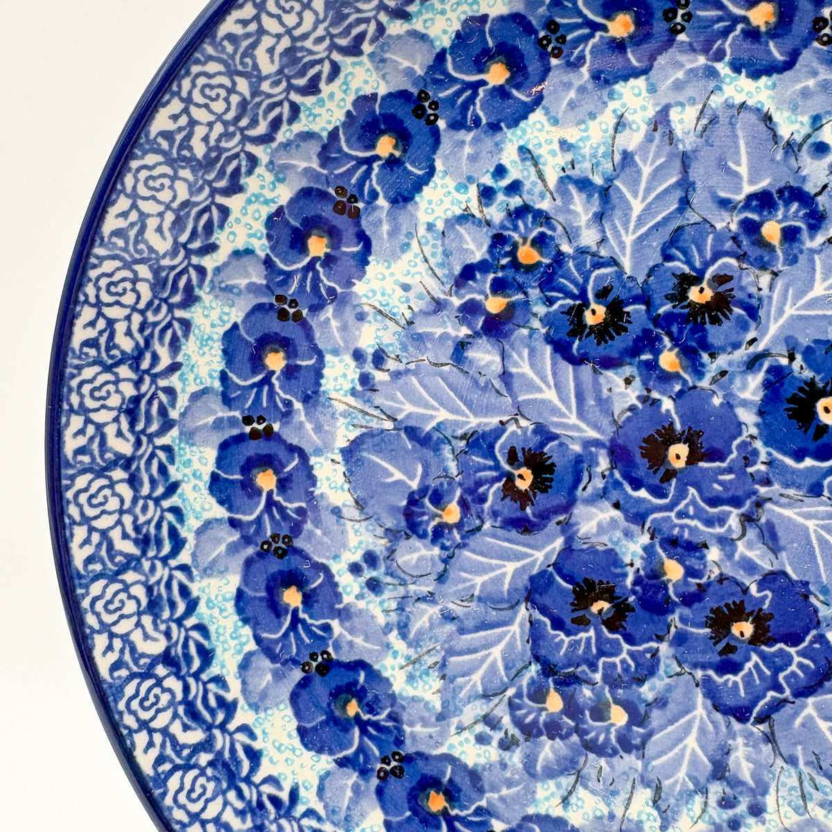 UNIKAT Deep Winter plate, close-up rim detail showing rose border and blue pansy petals