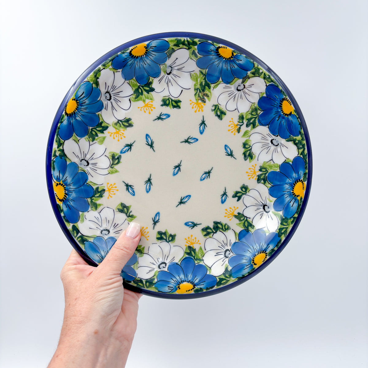 UNIKAT Blue Petal Dance plate held in hand, front view showing blue and white daisy ring