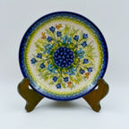 UNIKAT Bluebell Meadow plate, front view displayed on wooden stand showing blue bellflower burst and bees