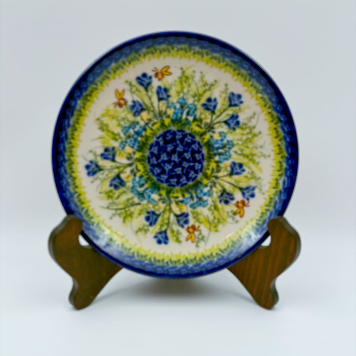 UNIKAT Bluebell Meadow plate, front view displayed on wooden stand showing blue bellflower burst and bees