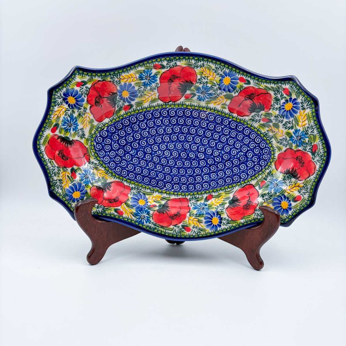 UNIKAT Garden Poppy Cezar platter, front view on stand showing red poppy border around blue spiral center