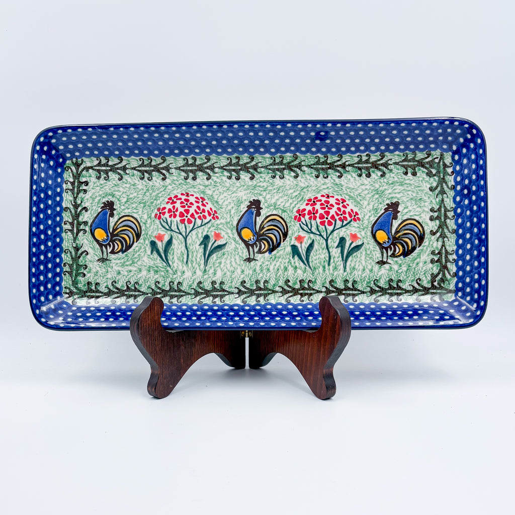 UNIKAT Rooster Dance rectangular platter, front view displayed on wooden stand showing roosters and pom-pom flowers