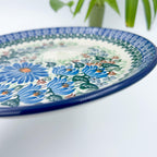UNIKAT Blue Beauty plate, close-up angled rim view showing blue daisy cluster and leaves