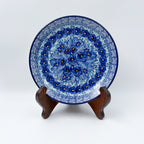 UNIKAT Deep Winter plate, front view displayed on wooden stand showing blue pansy cluster and rose border