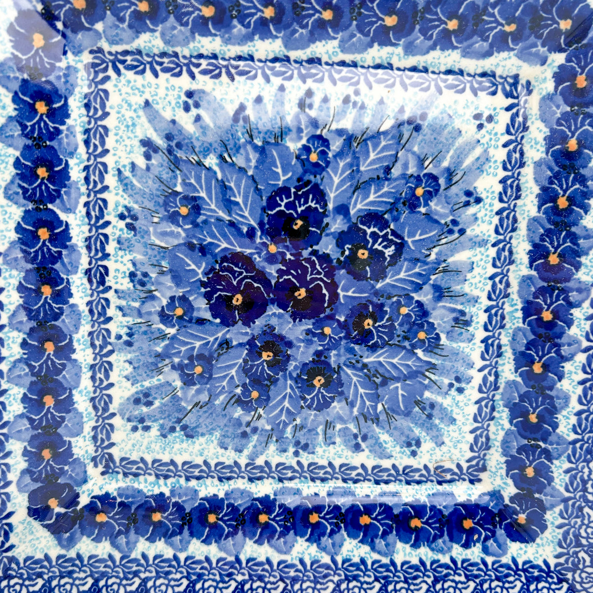 UNIKAT Deep Winter square plate, close-up top-down view of blue pansy bouquet center