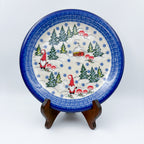 UNIKAT Gnome Village plate, front view displayed on wooden stand showing two gnomes, cabin, and pine trees