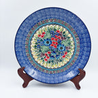 UNIKAT Splendid Meadow plate, front view displayed on wooden stand showing red and blue floral bouquet