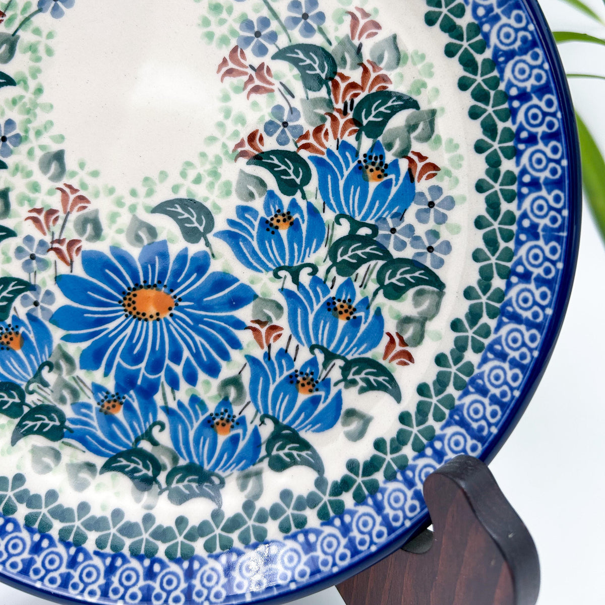 UNIKAT Blue Beauty plate, close-up view of blue daisy cluster and rim border displayed on stand