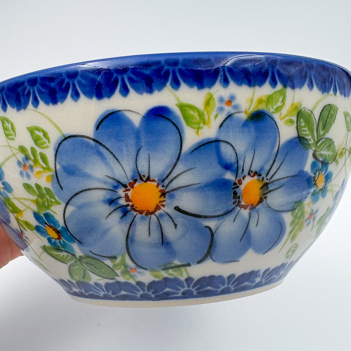 Blue Daisy bowl, close-up exterior view held in hand showing blue daisy flowers and leaves