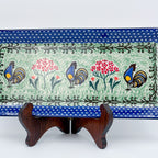 UNIKAT Rooster Dance rectangular platter, angled front view on stand showing three roosters and pom-pom flowers