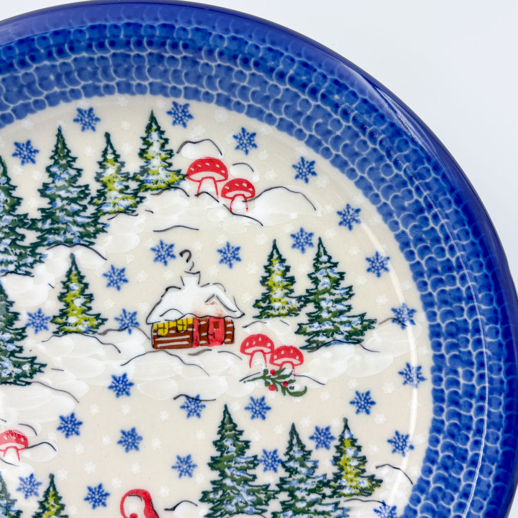 UNIKAT Gnome Village plate, close-up rim view showing snowy cabin and pine trees with mushrooms