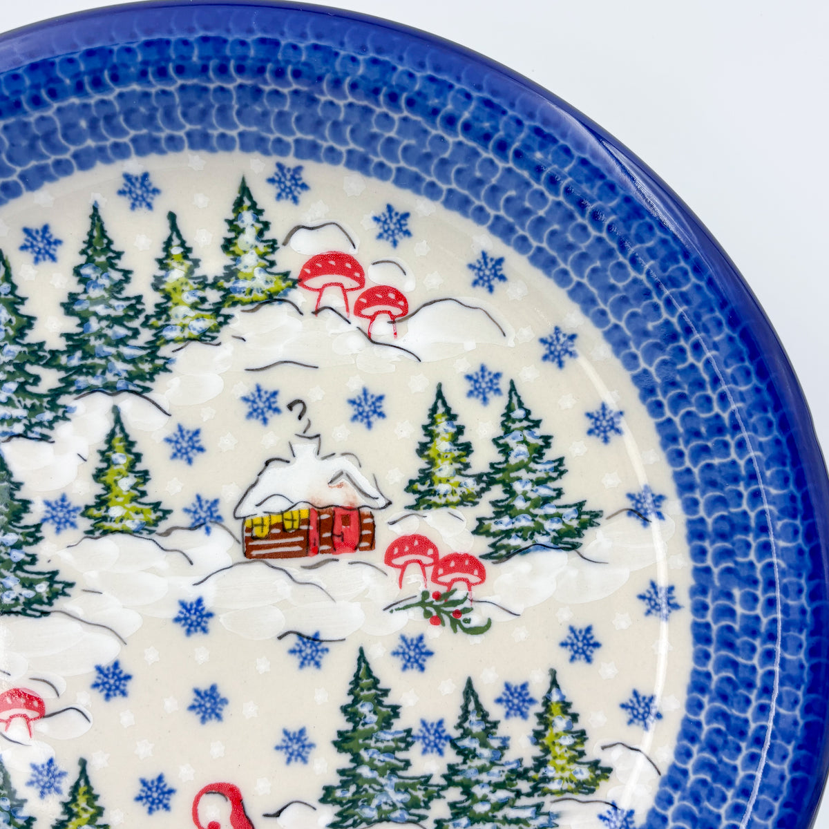 UNIKAT Gnome Village plate, close-up rim view showing snowy cabin and pine trees with mushrooms