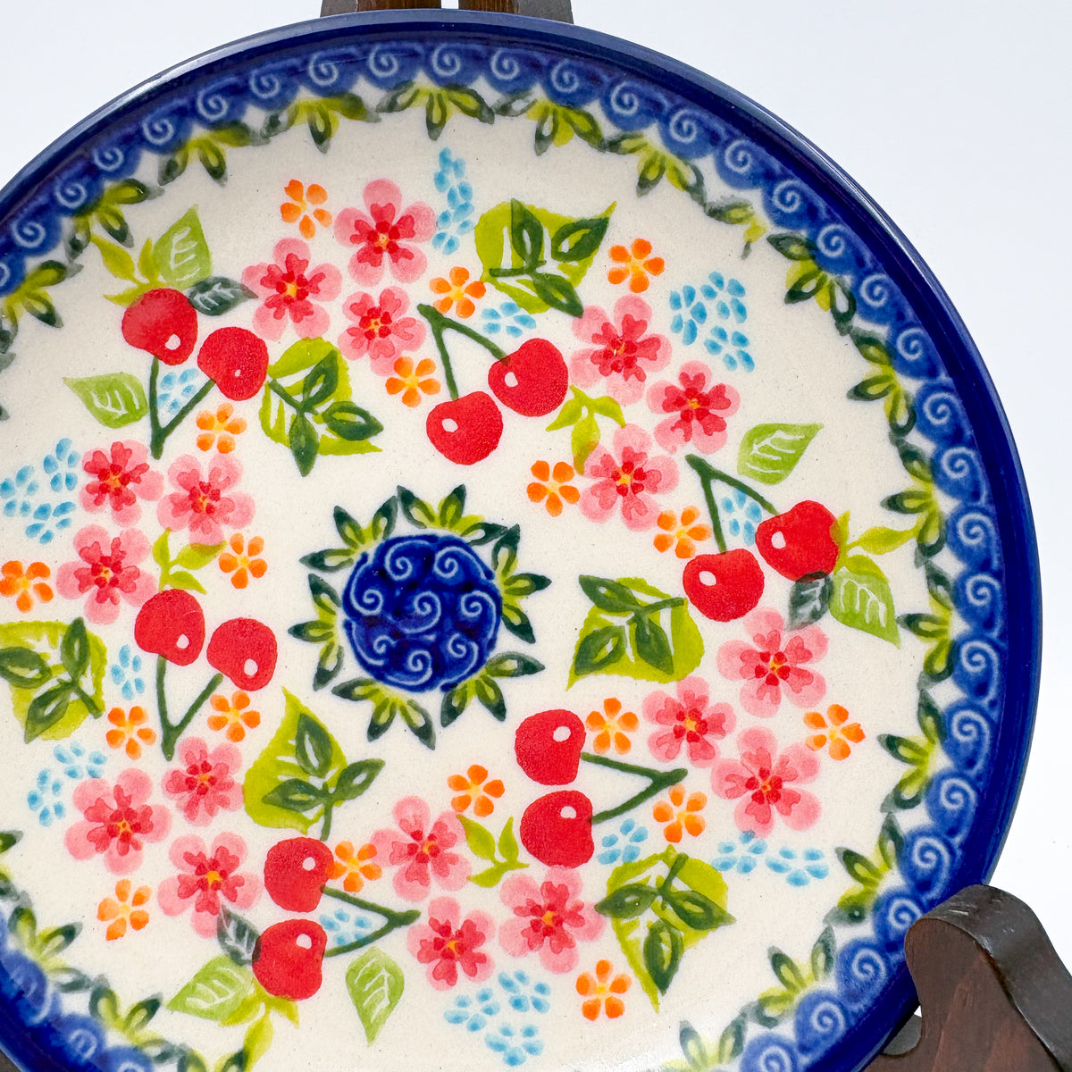 UNIKAT Cherry Blossom plate, close-up top-down view of red cherries and pink blossoms around blue spiral center