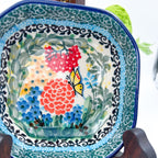 Close-up angled view of butterfly and floral center on Butterfly Garden square bowl, on display stand