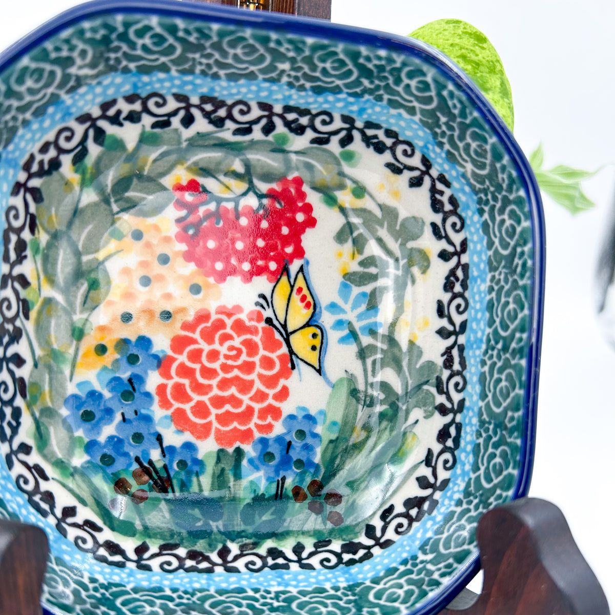 Close-up angled view of butterfly and floral center on Butterfly Garden square bowl, on display stand