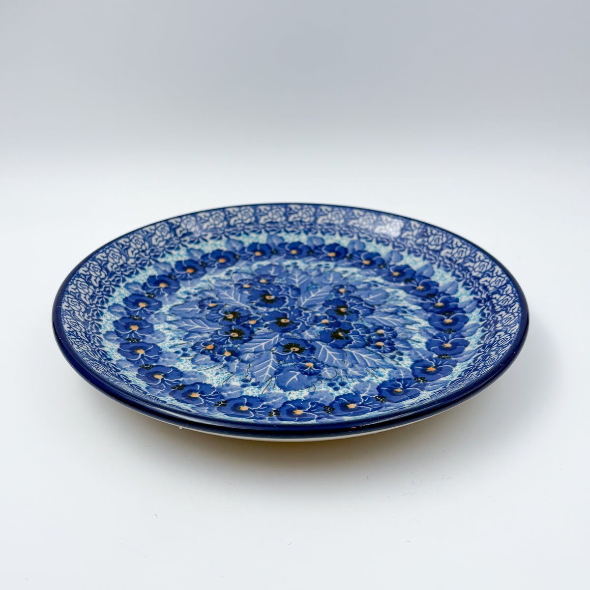 UNIKAT Deep Winter plate, front view showing blue pansy cluster on scalloped rim