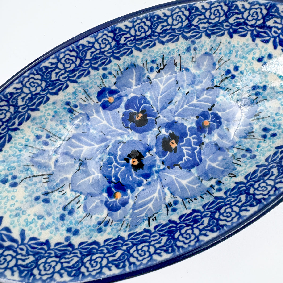 UNIKAT Deep Winter oval bowl, angled top-down close-up of blue pansy bouquet detail