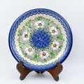 UNIKAT Primrose plate, front view displayed on wooden stand showing white poppy ring around blue dotted center