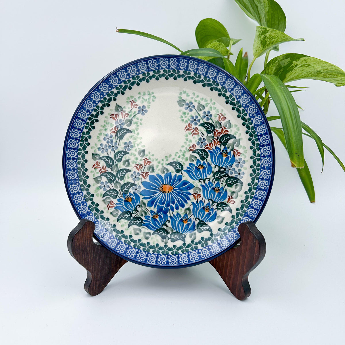 UNIKAT Blue Beauty plate, front view displayed on wooden stand showing blue daisy bouquet