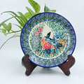 UNIKAT Hummingbird Meadow plate, front view displayed on wooden stand showing hummingbird and floral bouquet