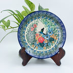 UNIKAT Hummingbird Meadow plate, front view displayed on wooden stand showing hummingbird and floral bouquet