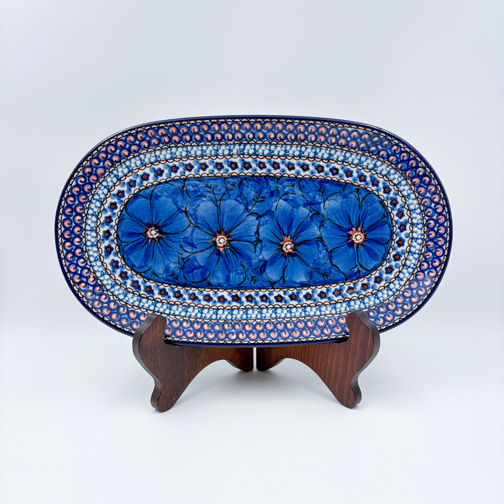 Cobalt Poppies oval platter, front view on stand showing row of blue poppy flowers and dotted mosaic border