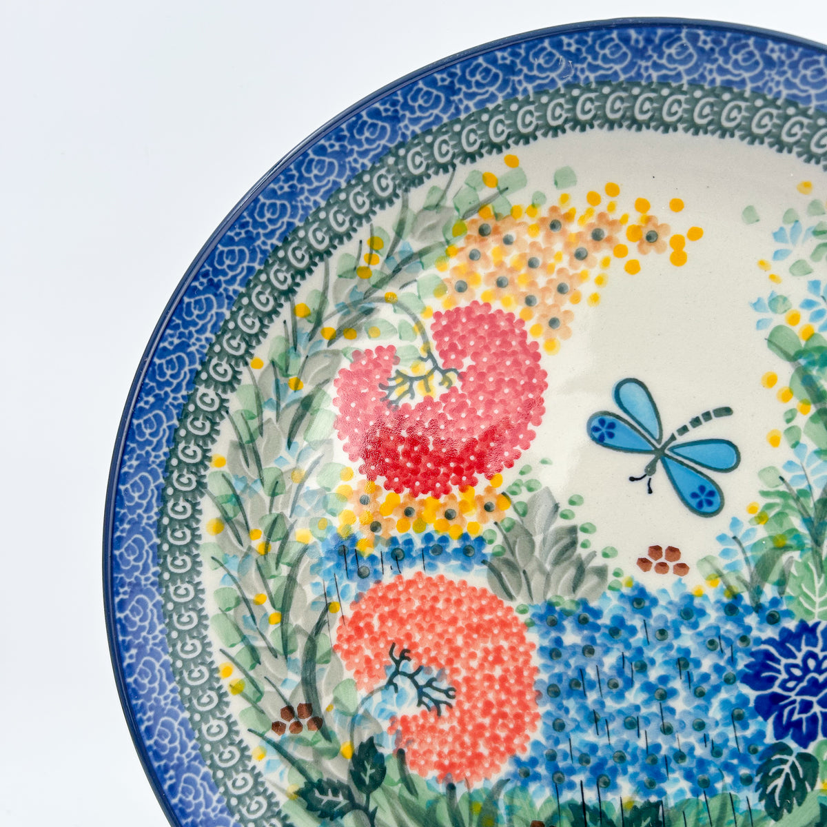 UNIKAT Garden Delight plate, close-up rim view showing pink pom-pom flower and blue dragonfly