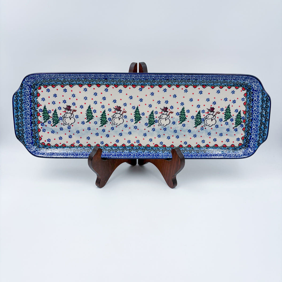 UNIKAT Snowman Stroll rectangular platter with handles, front view on stand showing snowmen and pine trees