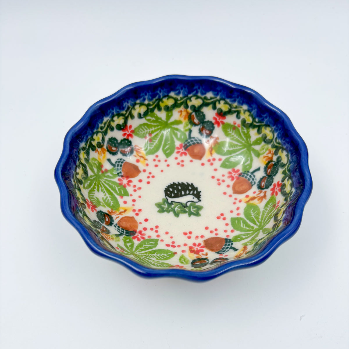 UNIKAT Hedgehog and Pumpkin scalloped bowl, top-down view showing hedgehog center with autumn leaf and acorn border