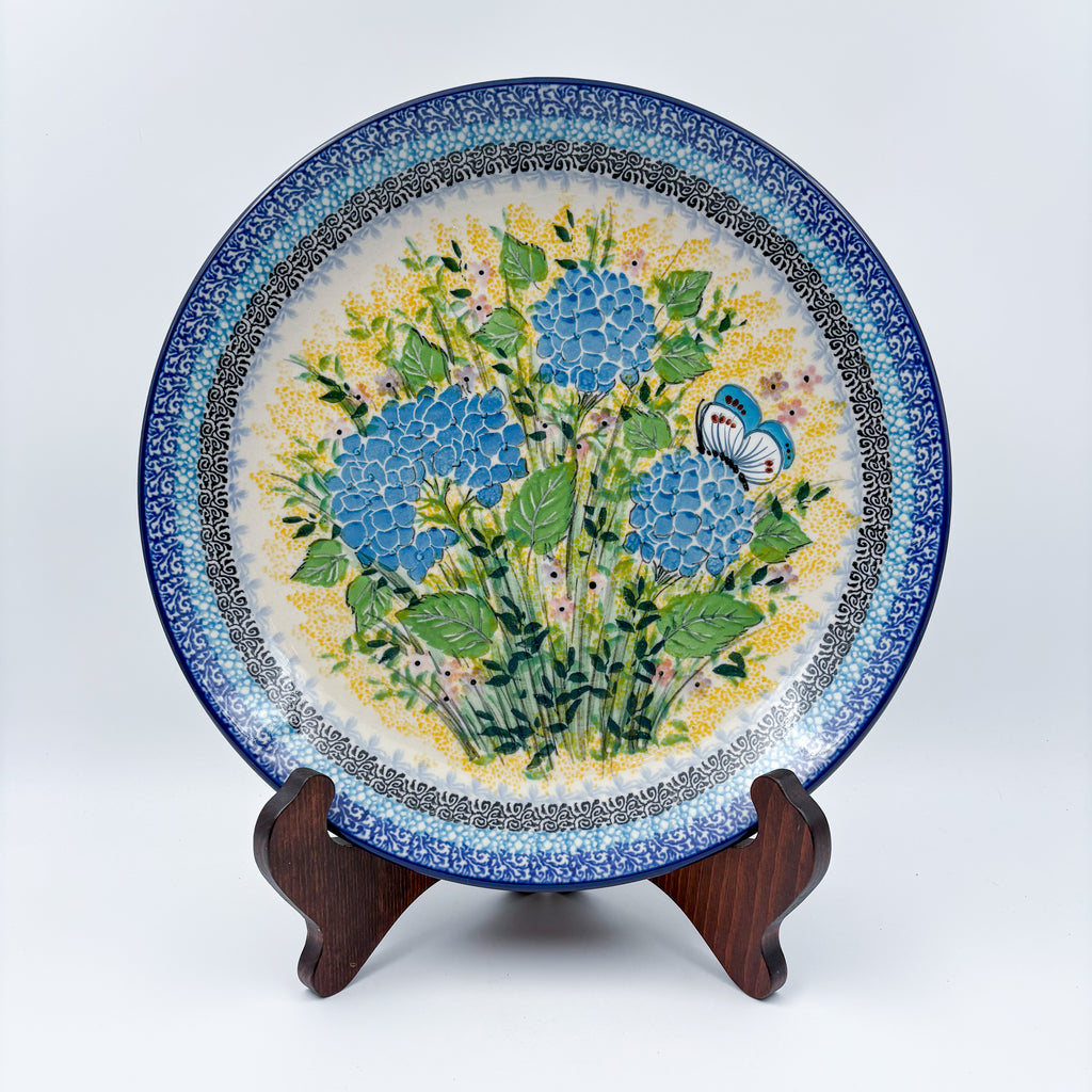 UNIKAT Blue Hydrangea plate, front view displayed on wooden stand showing blue hydrangea bouquet and butterfly