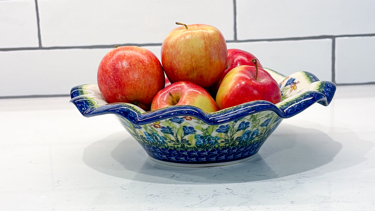 Red apples in a ruffled Polish pottery bowl painted with blue flowers, on a white kitchen counter