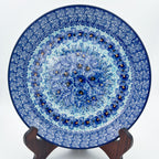 UNIKAT Deep Winter plate, front view displayed on wooden stand showing blue pansy ring and rose border